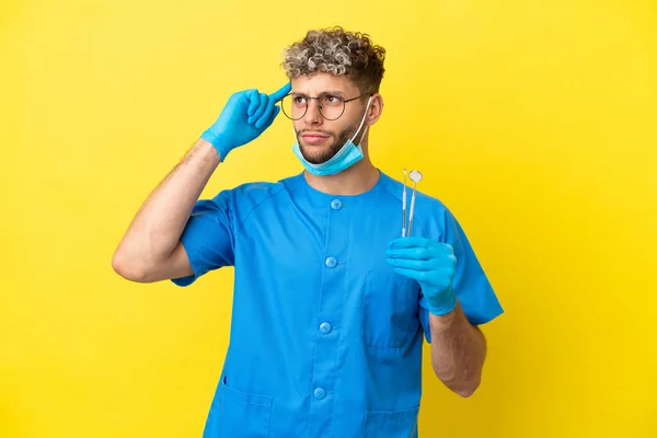 Dentysta Biały Mężczyzna Trzyma Narzędzia Izolowane Żółtym Tle Mając Wątpliwości — Zdjęcie stockowe