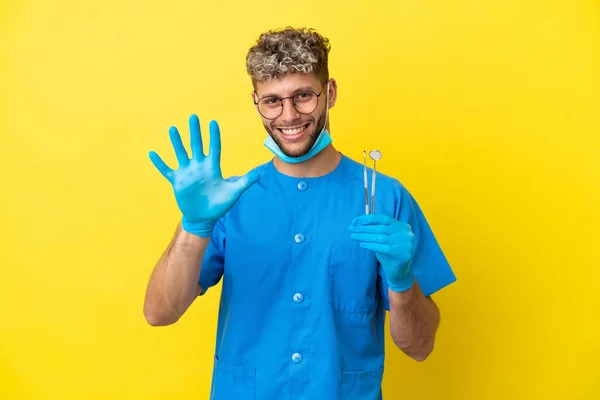 牙科医生高加索人拿着用黄色背景隔开的工具 用手指数着五个 — 图库照片