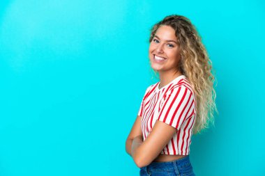 Kıvırcık saçlı kız mavi arka planda izole edilmiş, kolları bağlı ve ileriye bakıyor.