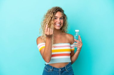 Mavi arka planda su şişesi olan genç sarışın kadın para hareketi yapıyor.
