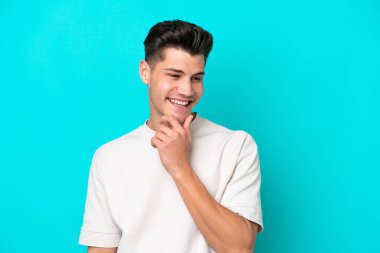 Genç, yakışıklı, beyaz bir adam, mavi bir bakkalda izole edilmiş, yan tarafa bakıyor ve gülümsüyor.