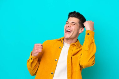 Genç, yakışıklı, beyaz bir adam mavi bir bakkalda izole edilmiş bir şekilde zaferi kutluyor.