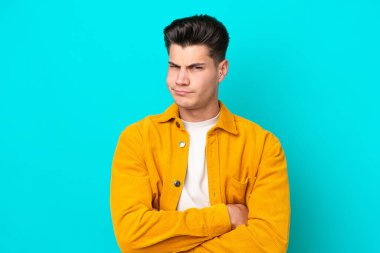 Young handsome caucasian man isolated on blue bakcground with unhappy expression