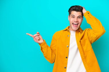 Genç, yakışıklı, beyaz bir adam mavi fırında izole edilmiş. Şaşırmış ve parmağıyla işaret ediyor.