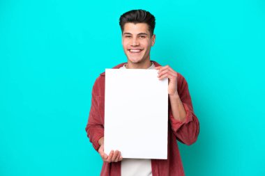 Genç, yakışıklı, beyaz bir adam mavi bir bakkalda izole edilmiş, elinde mutlu bir ifadeyle boş bir levha tutuyor.