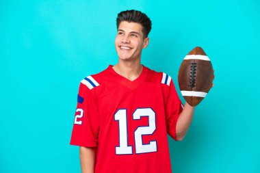 Rugby oynayan genç beyaz adam mavi arka planda izole edilmiş bir şekilde yukarı bakarken bir fikir düşünüyor.