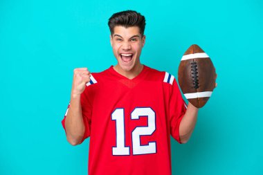 Rugby oynayan Kafkasyalı genç adam mavi arka planda tek başına galibiyetini kutluyor.