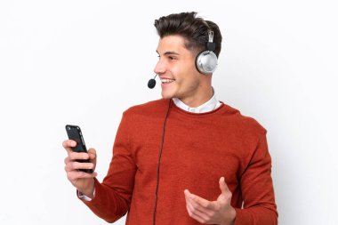 Beyaz arka planda izole edilmiş bir kulaklıkla çalışan beyaz pazarlamacı, cep telefonuyla konuşan biriyle konuşuyor.