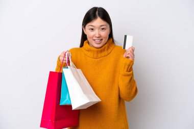 Beyaz arka planda izole edilmiş genç bir Çinli kadın elinde alışveriş çantaları ve bir kredi kartı tutuyor.