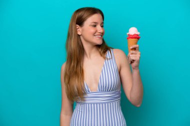 Mavi arka planda, mutlu bir ifadeyle izole edilmiş, mayo giymiş, dondurma yiyen beyaz bir kadın.