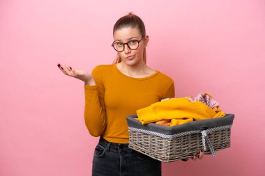 Pembe arka planda izole edilmiş çamaşır sepetini tutan genç beyaz kadın ellerini kaldırırken şüpheleri vardı.