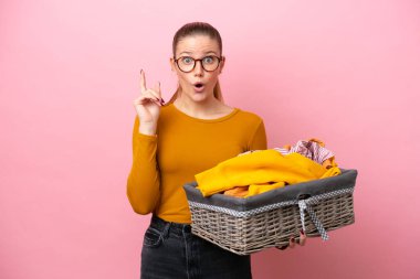 Pembe arka planda izole edilmiş çamaşır sepetini tutan beyaz bir kadın çözümün farkına varmak için parmağını kaldırıyor.