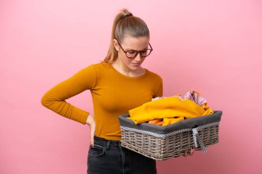 Pembe arka planda çamaşır sepeti tutan beyaz bir kadın gayret gösterdiği için sırt ağrısından muzdarip.