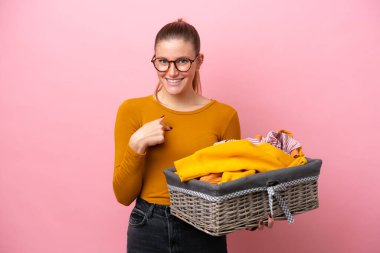 Pembe arka planda, yüzünde sürpriz bir ifadeyle izole edilmiş çamaşır sepeti tutan beyaz bir kadın.