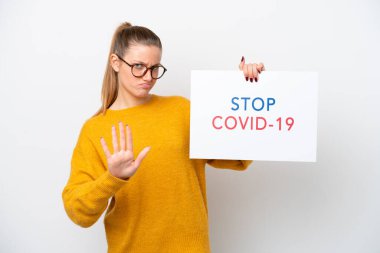 Young caucasian woman isolated on white background holding a placard with text Stop Covid 19 and doing stop sign
