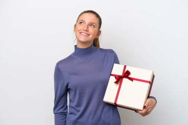 Beyaz arka planda izole edilmiş bir hediye tutan beyaz bir kadın gülümserken yukarı bakıyor.