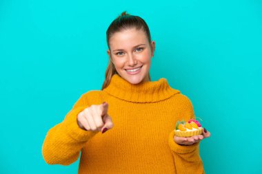 Mavi arka planda izole edilmiş turta tutan beyaz bir kadın kendinden emin bir ifadeyle seni işaret ediyor.
