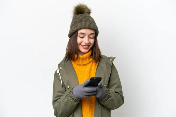 若いウクライナの女性は白い背景に隔離された冬のジャケットを着て携帯電話でメッセージを送信 — ストック写真