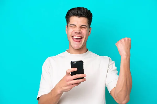 Junger Gutaussehender Kaukasier Isoliert Auf Blauem Bakcground Mit Telefon Siegesposition — Stockfoto