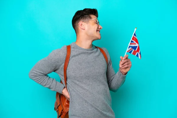 年轻的高加索男子举着一面英国国旗 蓝色背景孤立 背痛难忍 因为他付出了努力 — 图库照片