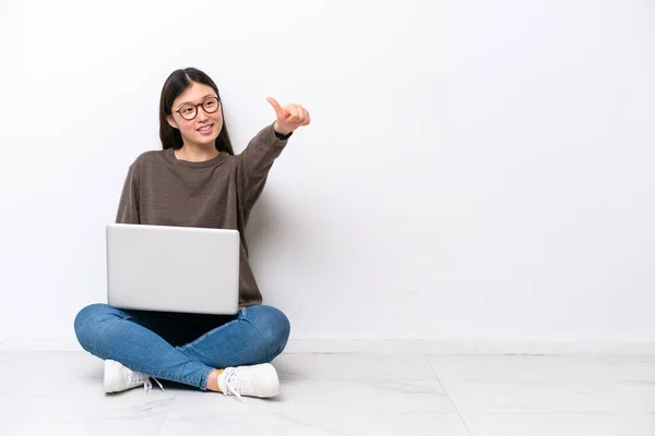 一个拿着笔记本电脑坐在地板上的年轻女人举起了一个大拇指 — 图库照片