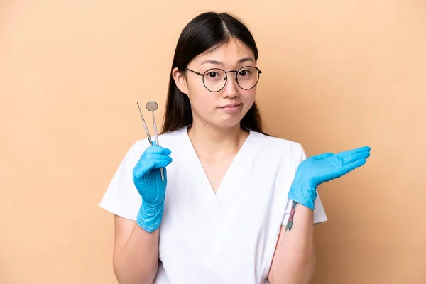 牙科医生中国妇女举手时 手持因米色背景而隔离的工具 但仍有疑问 — 图库照片