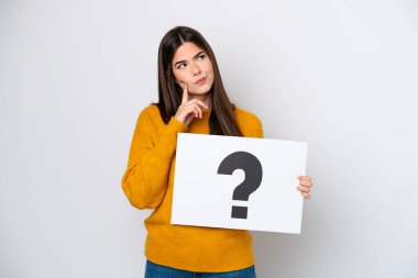 Beyaz arka planda izole edilmiş genç Brezilyalı bir kadın soru işareti olan bir pankart tutuyor ve düşünüyor.