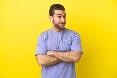 Sarışın, yalıtılmış sarı arka planda yakışıklı bir adam. Omuzlarını kaldırırken şüpheli hareketler yapıyor.