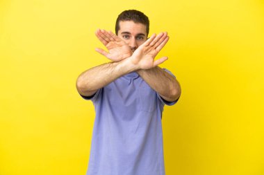 Sarışın, izole edilmiş sarı arka planda yakışıklı bir adam. Bir hareketi durdurmak için el hareketi yapıyor.