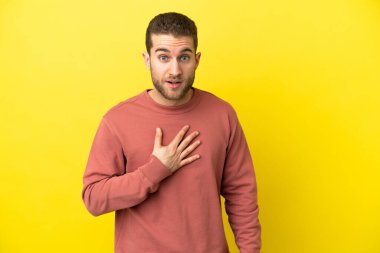 Sarışın yakışıklı adam, izole edilmiş sarı arka planda şaşırmış ve şaşırmış görünüyor.