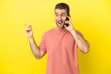 Yakışıklı sarışın adam izole arka planda cep telefonu kullanıyor. Çözümü bulmak için parmağını kaldırıyor.