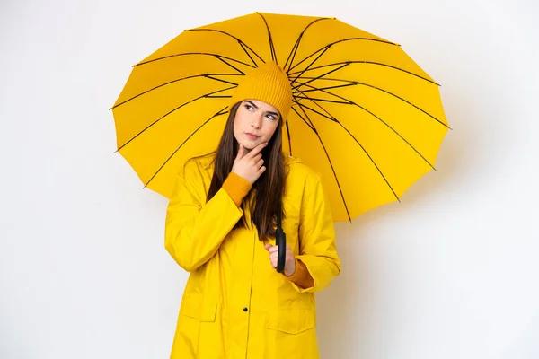 若いですブラジル人女性でレインプルーフコートと傘は白い背景に隔離されて疑問を持って — ストック写真