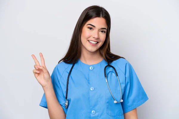 白を背景に孤立した若いブラジル人看護師の女性笑顔と勝利のサインを示す — ストック写真