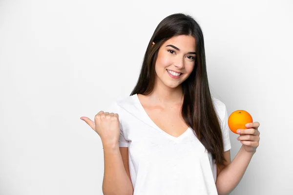 Молодая Бразильская Женщина Держит Апельсин Изолирован Белом Фоне Указывая Сторону — стоковое фото
