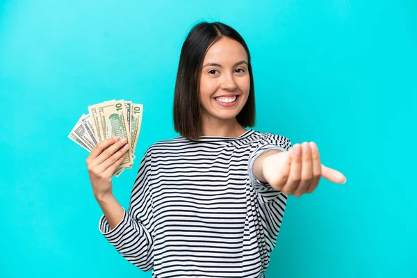 Young caucasian woman taking a lot of money isolated on blue background inviting to come with hand. Happy that you came