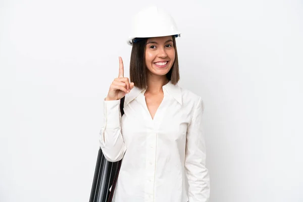 年轻的女建筑师 戴着头盔 拿着用白色背景隔开的设计图 展示并举起一个手指 表示她是最优秀的建筑师 — 图库照片