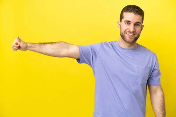 一个漂亮的金发男人 在孤立的黄色背景上举起大拇指 做一个手势 — 图库照片