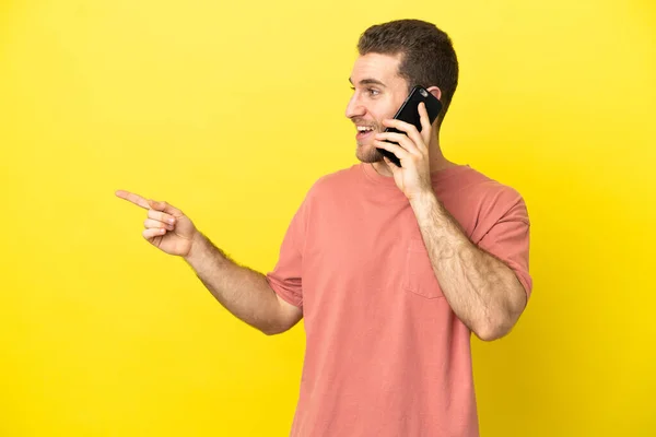 Przystojny Blondynka Człowiek Pomocą Telefonu Komórkowego Odosobnionym Tle Wskazując Palcem — Zdjęcie stockowe