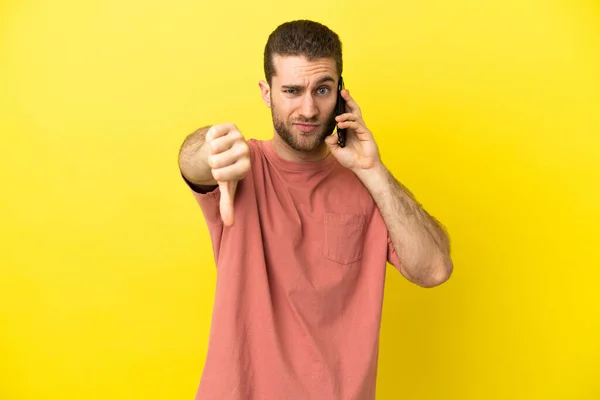 Przystojny Blondynka Człowiek Pomocą Telefonu Komórkowego Odosobnionym Tle Pokazuje Kciuk — Zdjęcie stockowe
