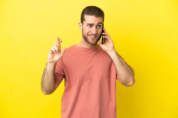 Handsome Blonde Man Using Mobile Phone Isolated Background Fingers Crossing — Zdjęcie stockowe