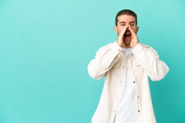 Yakışıklı sarışın adam izole edilmiş mavi arka planda bağırıyor ve bir şeyler söylüyor.