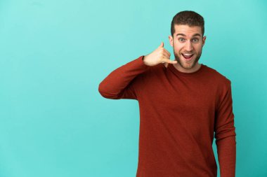 Soyutlanmış mavi arka planda yakışıklı sarışın bir adam telefon jesti yapıyor. Bana geri dönüş işareti ver.