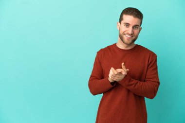 Yakışıklı sarışın adam izole edilmiş mavi arka planda alkışlıyor.