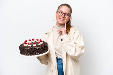 Beyaz arka planda izole edilmiş bir doğum günü pastası tutan beyaz bir kadın yukarı bakarken bir fikir düşünüyor.