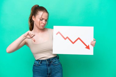 Young caucasian woman isolated on green background holding a sign with a decreasing statistics arrow symbol and doing bad signal