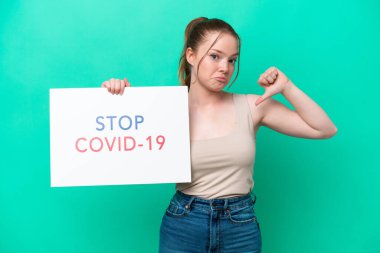 Kafkasyalı genç bir kadın yeşil arka planda izole edilmiş. Elinde yazılı bir levha var. Covid 19 'u gururla durdurun.