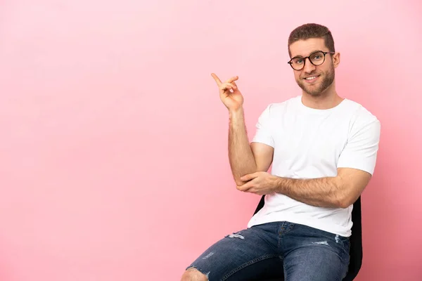 Young Man Sitting Chair Isolated Pink Background Pointing Finger Side — Stock fotografie