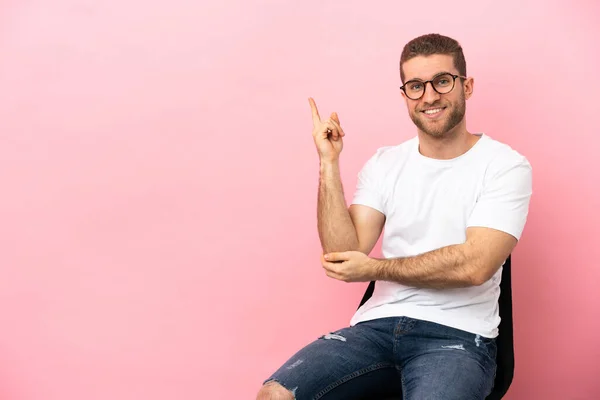 Young Man Sitting Chair Isolated Pink Background Happy Pointing — Stock fotografie