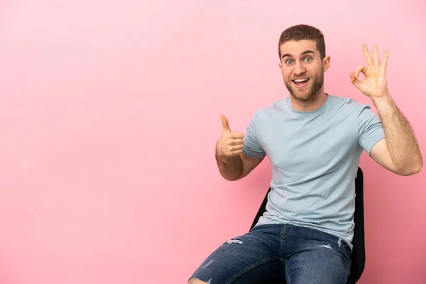 Young Man Sitting Chair Isolated Pink Background Showing Sign Thumb — Stockfoto