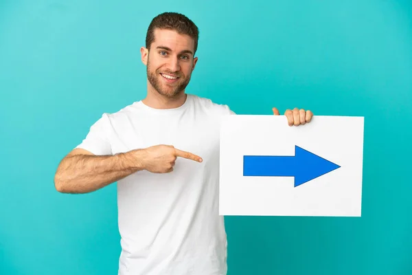 Handsome Blonde Man Isolated Blue Background Holding Placard Arrow Symbol — Stock Fotó